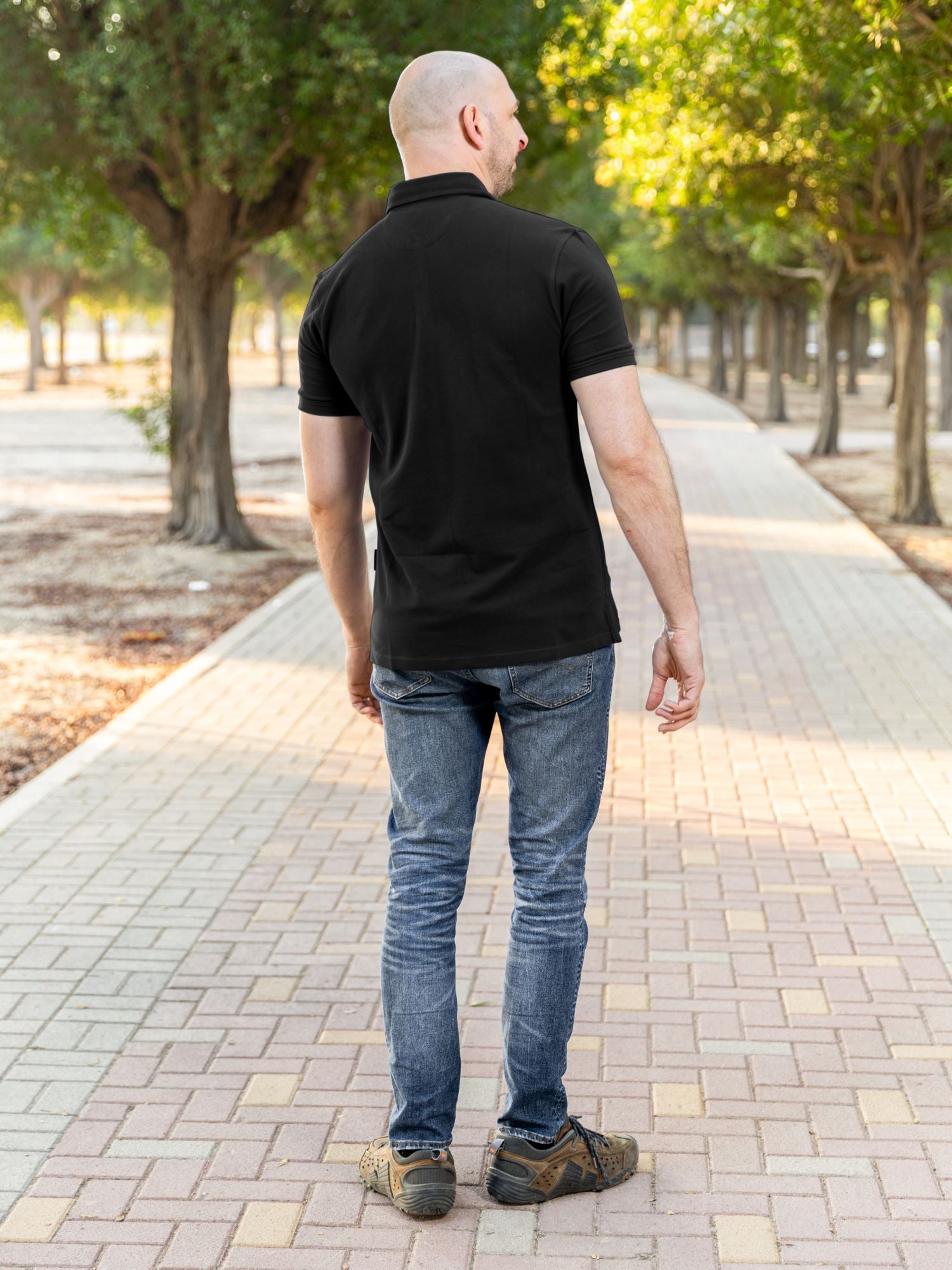 A shot from behind of a tall athletic guy in a park and wearing a black XL tall polo shirt.