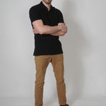 A head to toe shot of a tall skinny guy wearing an XL tall black pique polo shirt in a studio with hands folded.