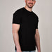 A tall and slim man in the studio standing in front of a light background. The smiling model is wearing an extra long slim black t-shirt in a size XL. The tall black t-shirt features a 3" longer body, 100% organic cotton, and is soft & preshrunk. The black t-shirt is ideal for tall slim men 6'2"+.