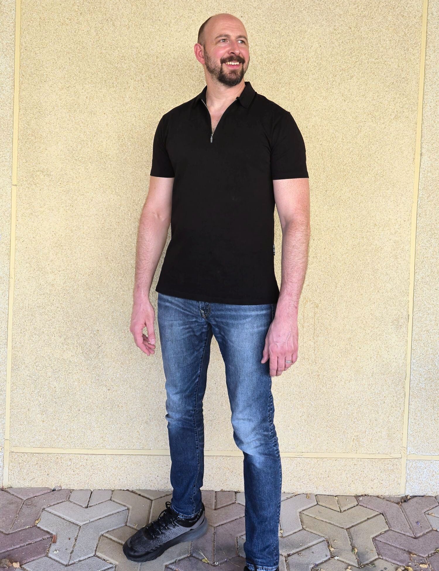 A head to toe shot of a tall slim guy wearing an XL tall black zip polo shirt.