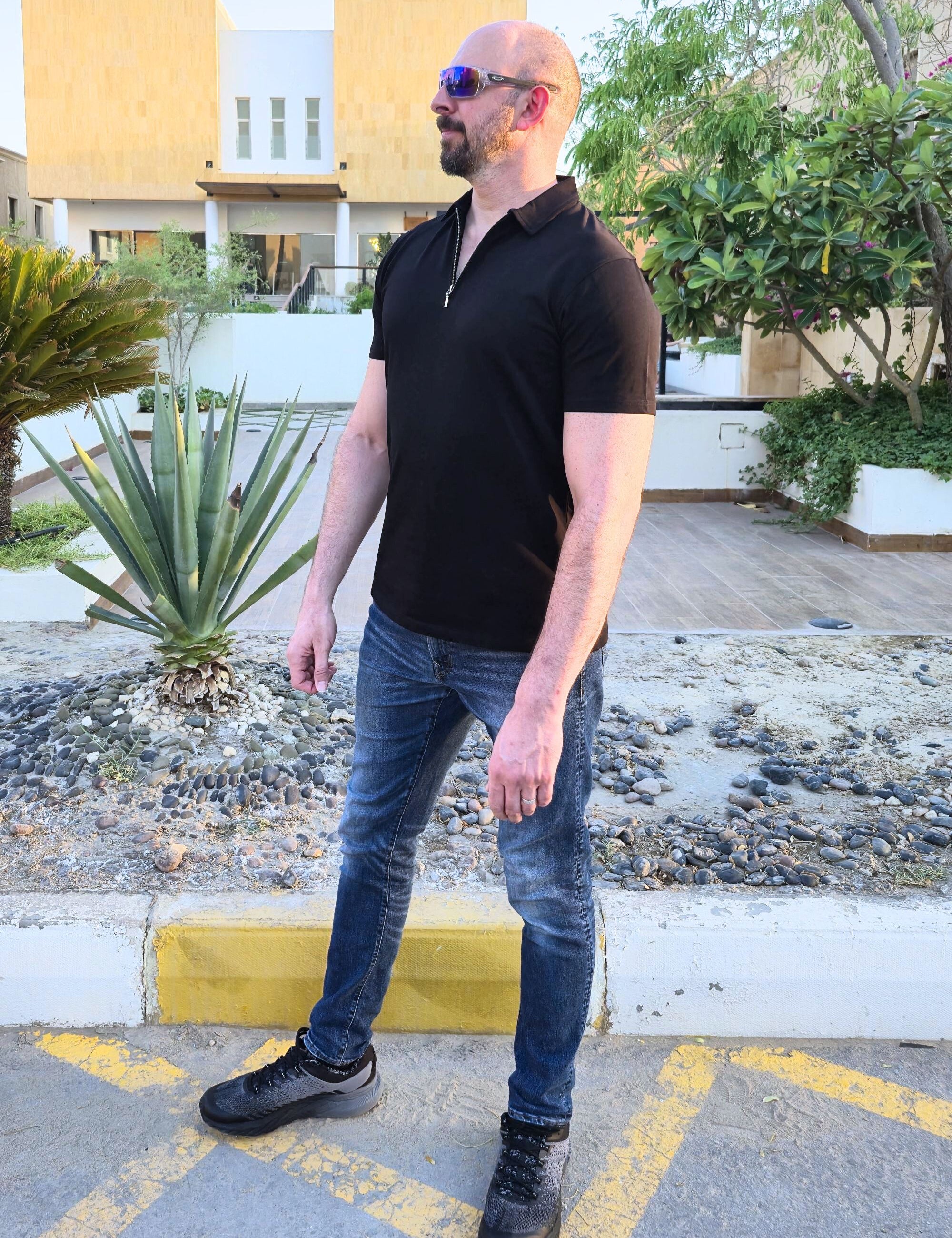 A head to toe shot of a tall slim man wearing an XL tall black zip polo shirt.