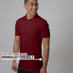 An upper body shot of a tall slim man standing and smiling in a studio and wearing a maroon medium tall polo shirt.