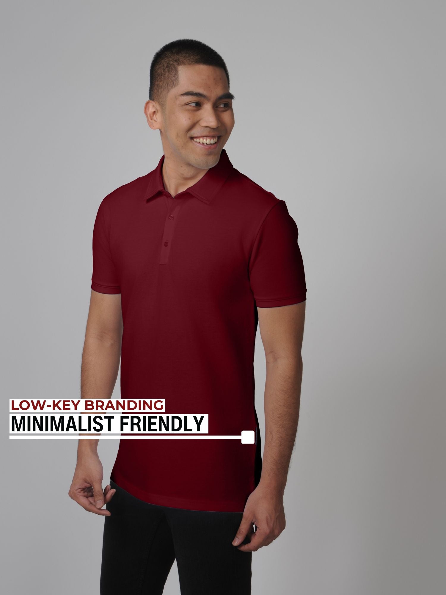 An upper body shot of a tall slim man standing and smiling in a studio and wearing a maroon medium tall polo shirt.