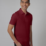 An upper body shot of a tall slim man standing in a studio and wearing a maroon medium tall polo shirt.