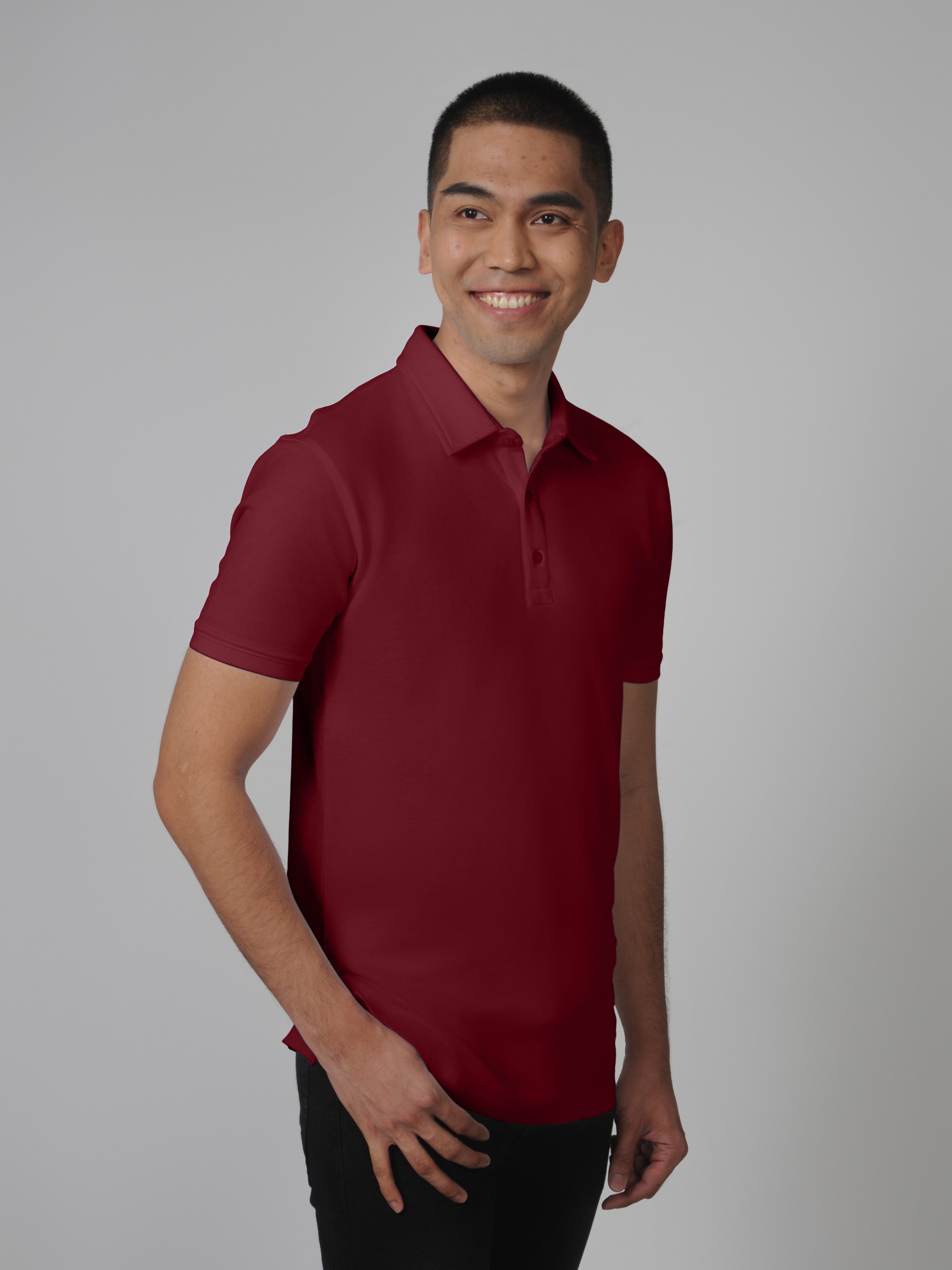 An upper body shot of a tall slim man standing in a studio and wearing a maroon medium tall polo shirt.