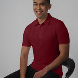 A tall slim man sitting in a studio and wearing a maroon medium tall polo shirt.