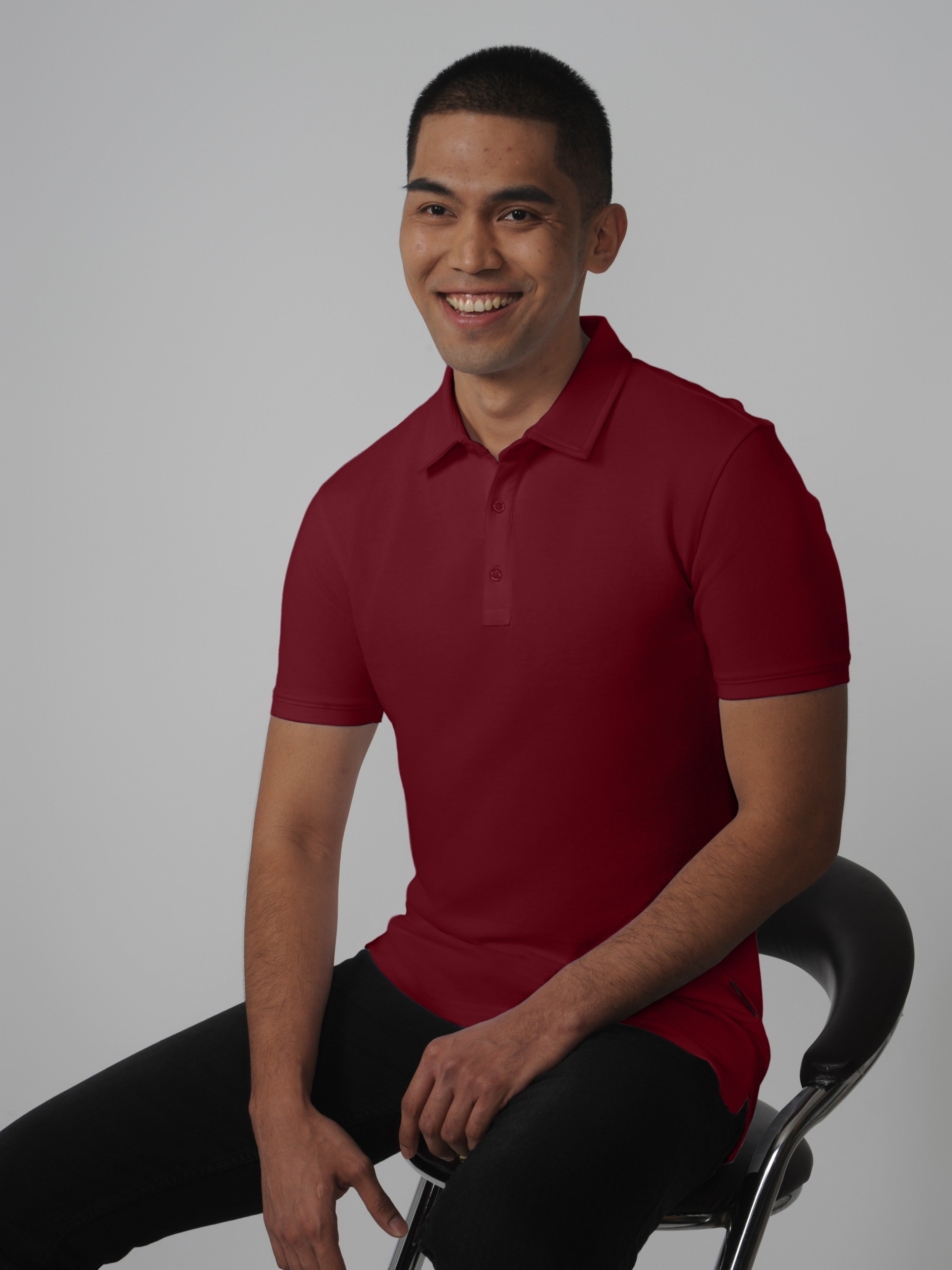 A tall slim man sitting in a studio and wearing a maroon medium tall polo shirt.