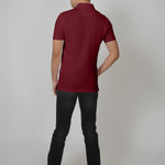 A shot from behind of a tall slim man standing in a studio and wearing a maroon medium tall polo shirt.