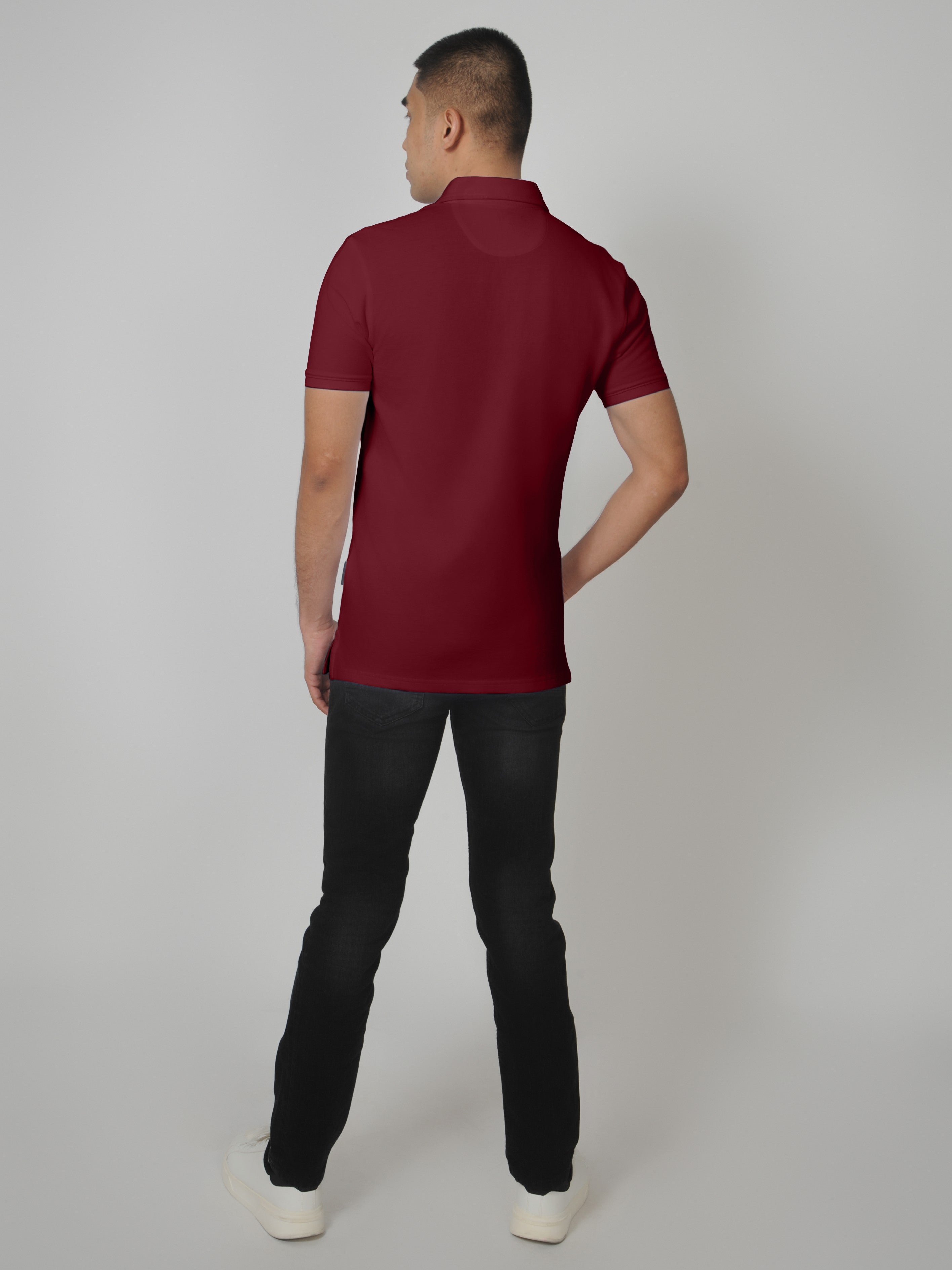 A shot from behind of a tall slim man standing in a studio and wearing a maroon medium tall polo shirt.