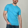 A tall and slim man in the studio standing in front of a light background with one hand in his pocket. The model is wearing an extra long slim cyan blue t-shirt in a size XL. The cyan blue t-shirt features a 3" longer body, 100% organic cotton, and is soft & preshrunk. The cyan blue t-shirt is ideal for tall slim men 6'2"+.