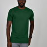 A tall and slim man in the studio standing in front of a light background. The model is wearing an extra long slim dark green t-shirt in a size large. The dark green t-shirt features a 3" longer body, 100% organic cotton, and is soft & preshrunk. The dark green t-shirt is ideal for tall slim men 6'2"+.