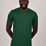 A tall and slim guy smiling in the studio, hands behind back and wearing a dark green L tall slim t-shirt.