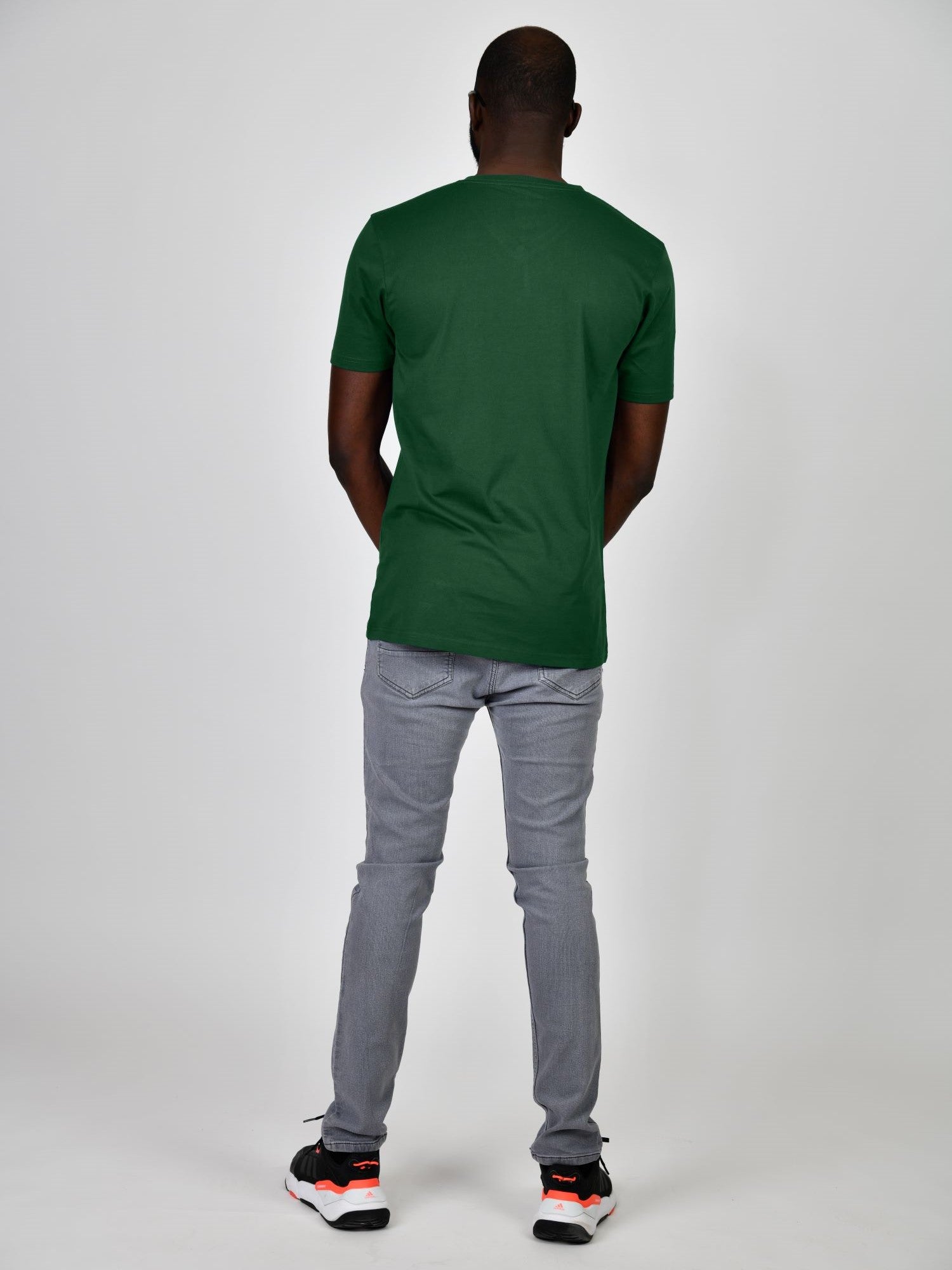 A shot from behind of a tall and slim guy in the studio and wearing a dark green L tall slim t-shirt.