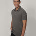 A tall and slim man in the studio standing in front of a light background. The smiling model is wearing an extra long slim dark grey polo shirt in a size medium. The tall dark grey polo shirt features a 3" longer body, 100% organic cotton, and is soft & preshrunk. The dark grey polo shirt is ideal for tall slim men 6'2"+.