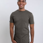 A tall and slim man in the studio standing in front of a light background. The smiling model is wearing an extra long slim dark grey t-shirt in a size medium. The tall dark grey t-shirt features a 3" longer body, 100% organic cotton, and is soft & preshrunk. The dark grey t-shirt is ideal for tall slim men 6'2"+.