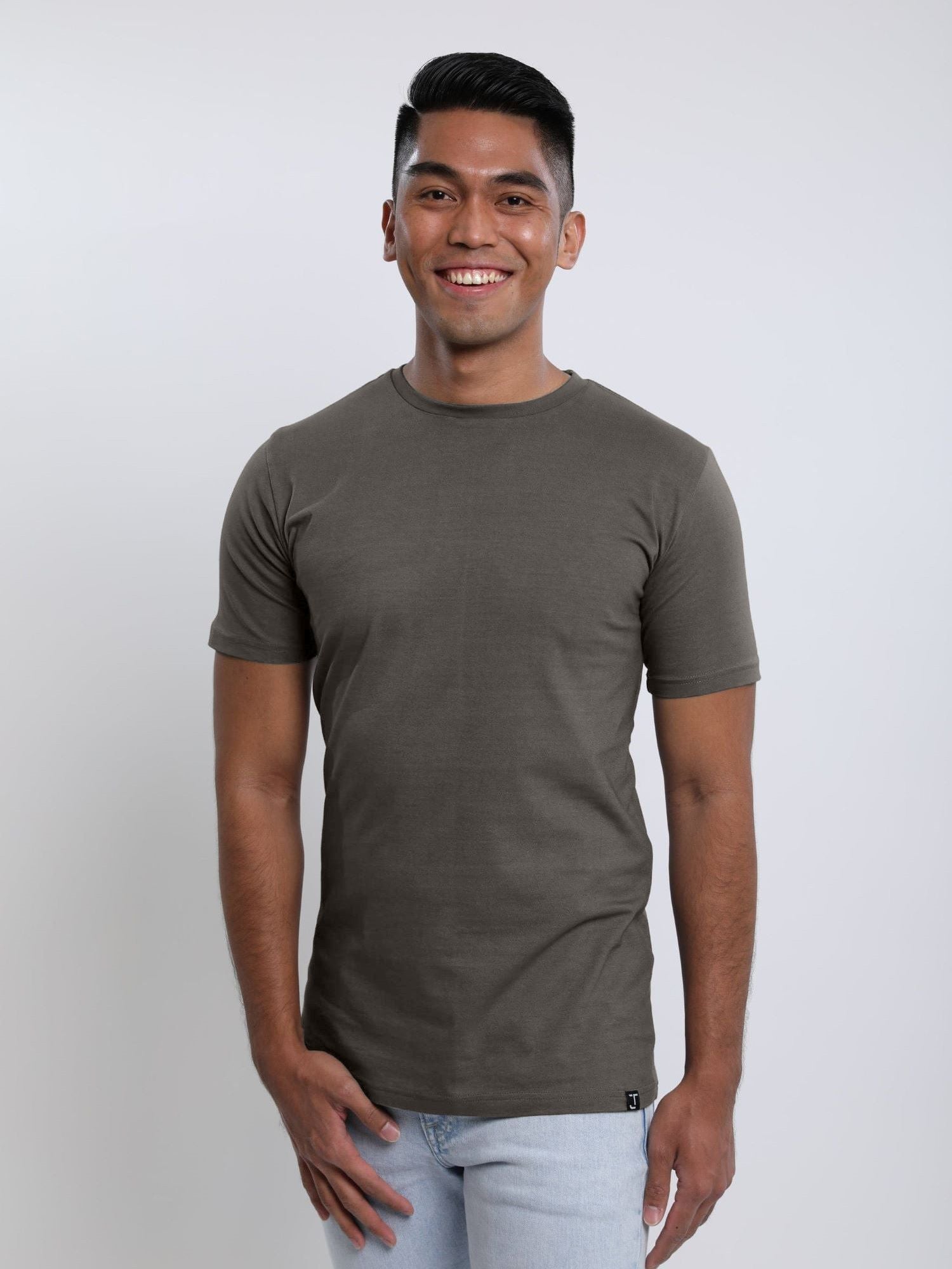 A tall and slim man in the studio standing in front of a light background. The smiling model is wearing an extra long slim dark grey t-shirt in a size medium. The tall dark grey t-shirt features a 3" longer body, 100% organic cotton, and is soft & preshrunk. The dark grey t-shirt is ideal for tall slim men 6'2"+.