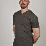 A tall and slim man in the studio standing in front of a light background with hands behind back. The smiling model is wearing an extra long slim dark grey v-neck t-shirt in a size XL. The tall dark grey v-neck t-shirt features a 3" longer body, 100% organic cotton, and is soft & preshrunk. The dark grey v-neck t-shirt is ideal for tall slim men 6'2"+.