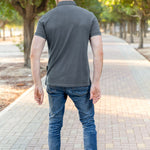 A shot from behind of a tall athletic guy in a park and wearing a dark slate XL tall polo shirt.