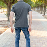 A shot from behind of a tall athletic guy in a park and wearing a dark slate XL tall polo shirt.