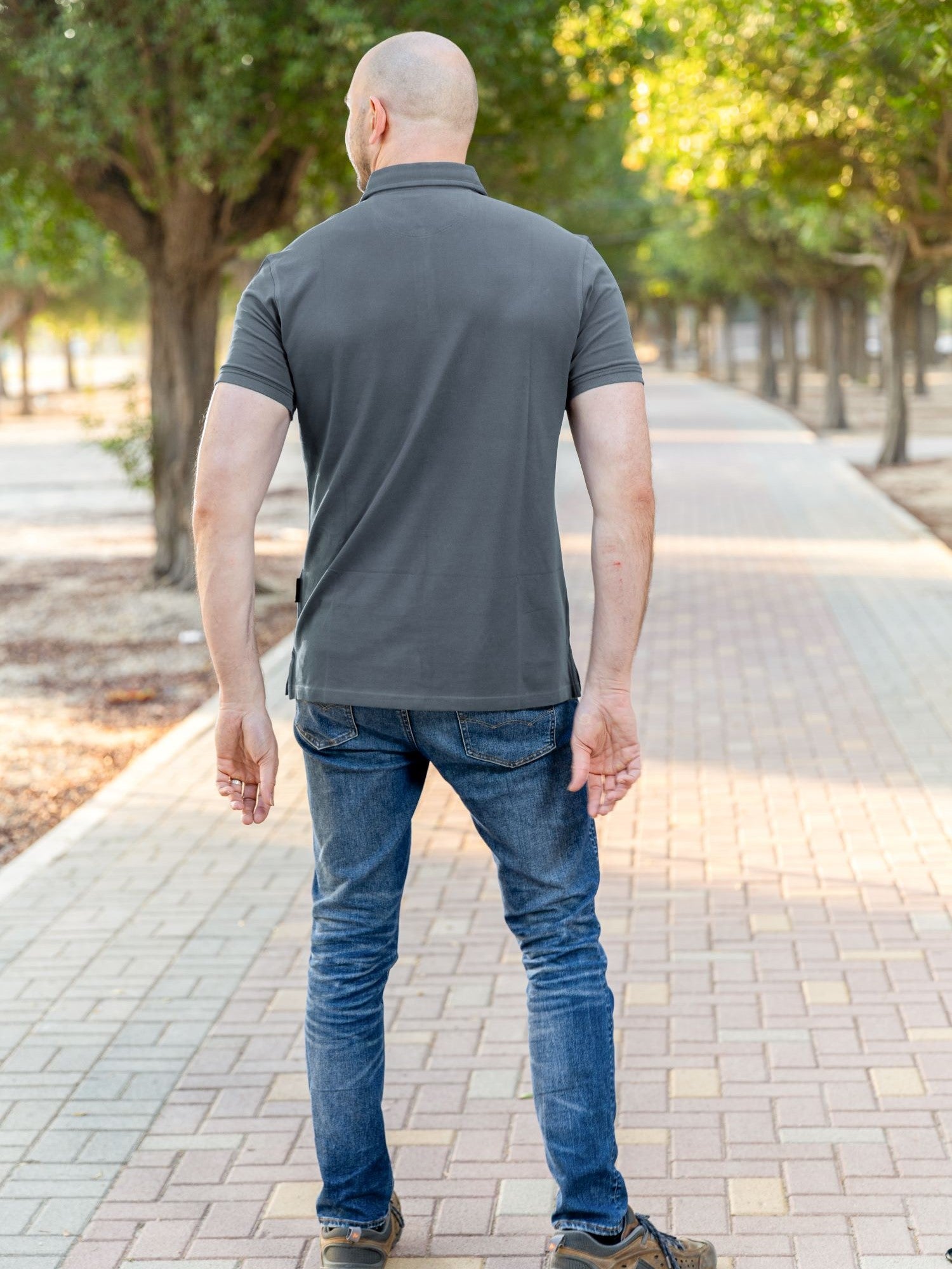 A shot from behind of a tall athletic guy in a park and wearing a dark slate XL tall polo shirt.