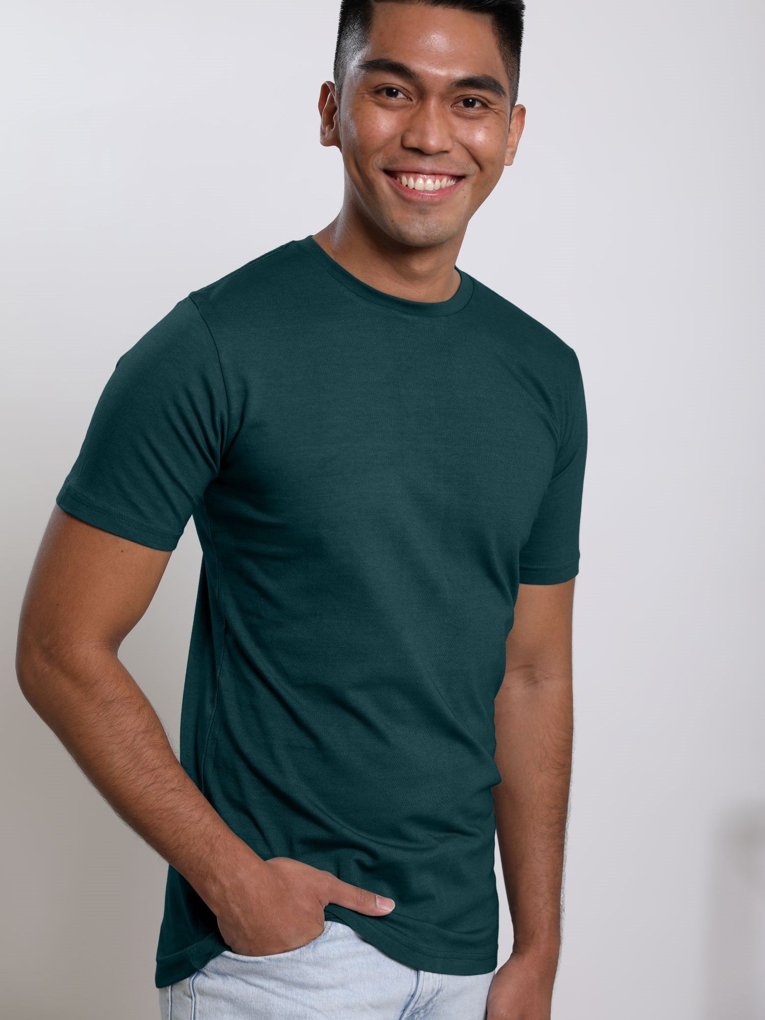 An upper body shot of a tall skinny guy wearing a dark teal medium tall t-shirt, hand in pocket.