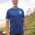 A tall and slim man standing by the sea. The smiling model is wearing a navy blue extra long graphic t-shirt with a minimal lake design. It features a 3" longer body, 100% organic cotton, and is soft & preshrunk. This extra long tall graphic tee is ideal for tall slim men 6'2"+