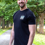 An upper body shot of a tall slim guy in a park wearing an XL tall and slim fitting graphic t-shirt in black.