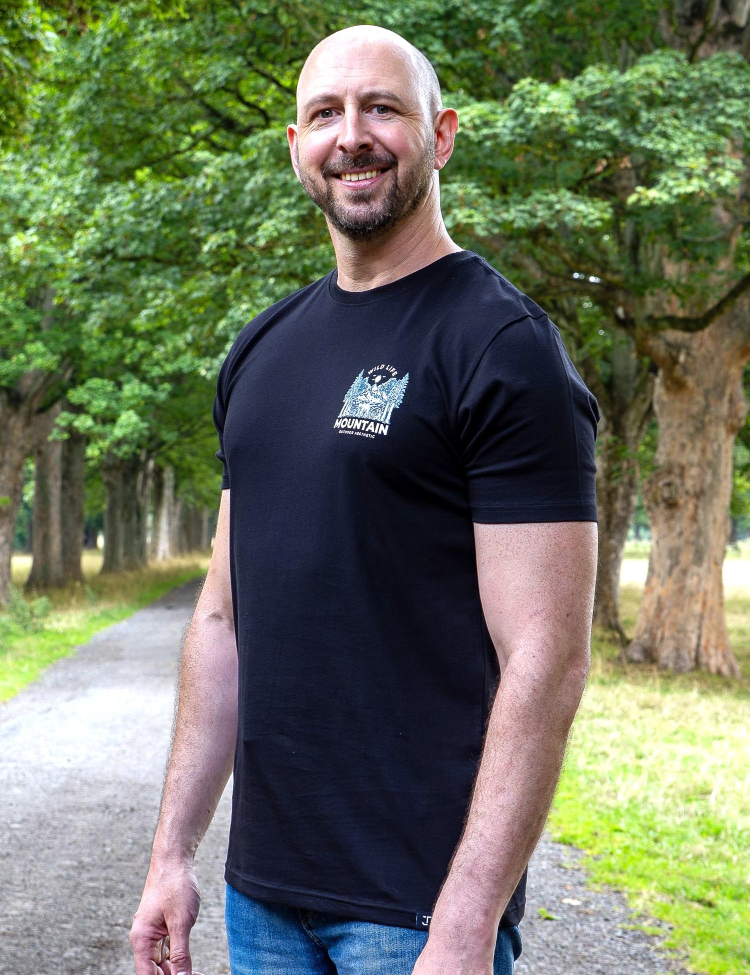 An upper body shot of a tall slim guy in a park wearing an XL tall and slim fitting graphic t-shirt in black.