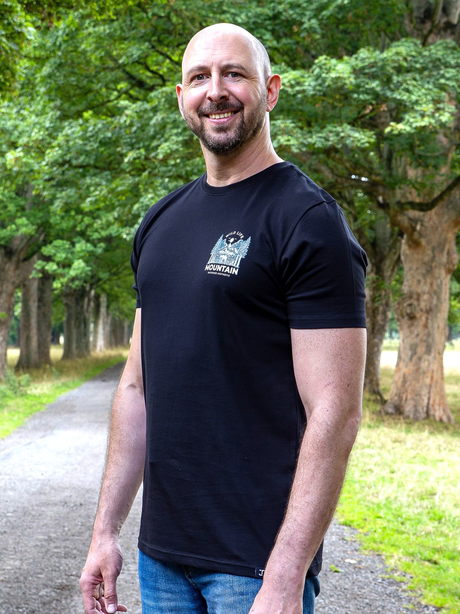 An upper body shot of a tall slim guy in a park wearing an XL tall and slim fitting graphic t-shirt in black.