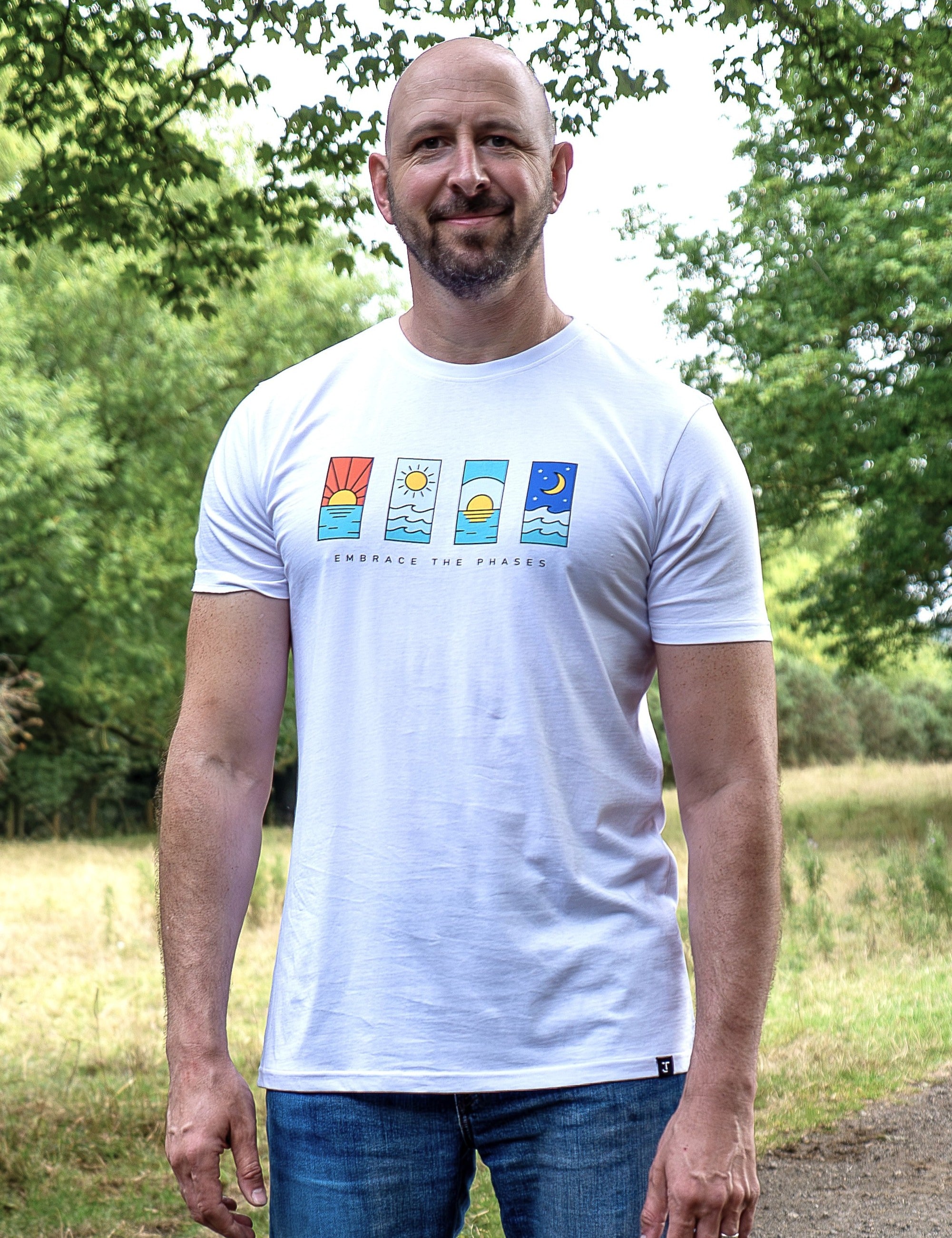 An upper body shot of a tall slim guy in a park wearing an XL tall and slim fitting graphic t-shirt in white.
