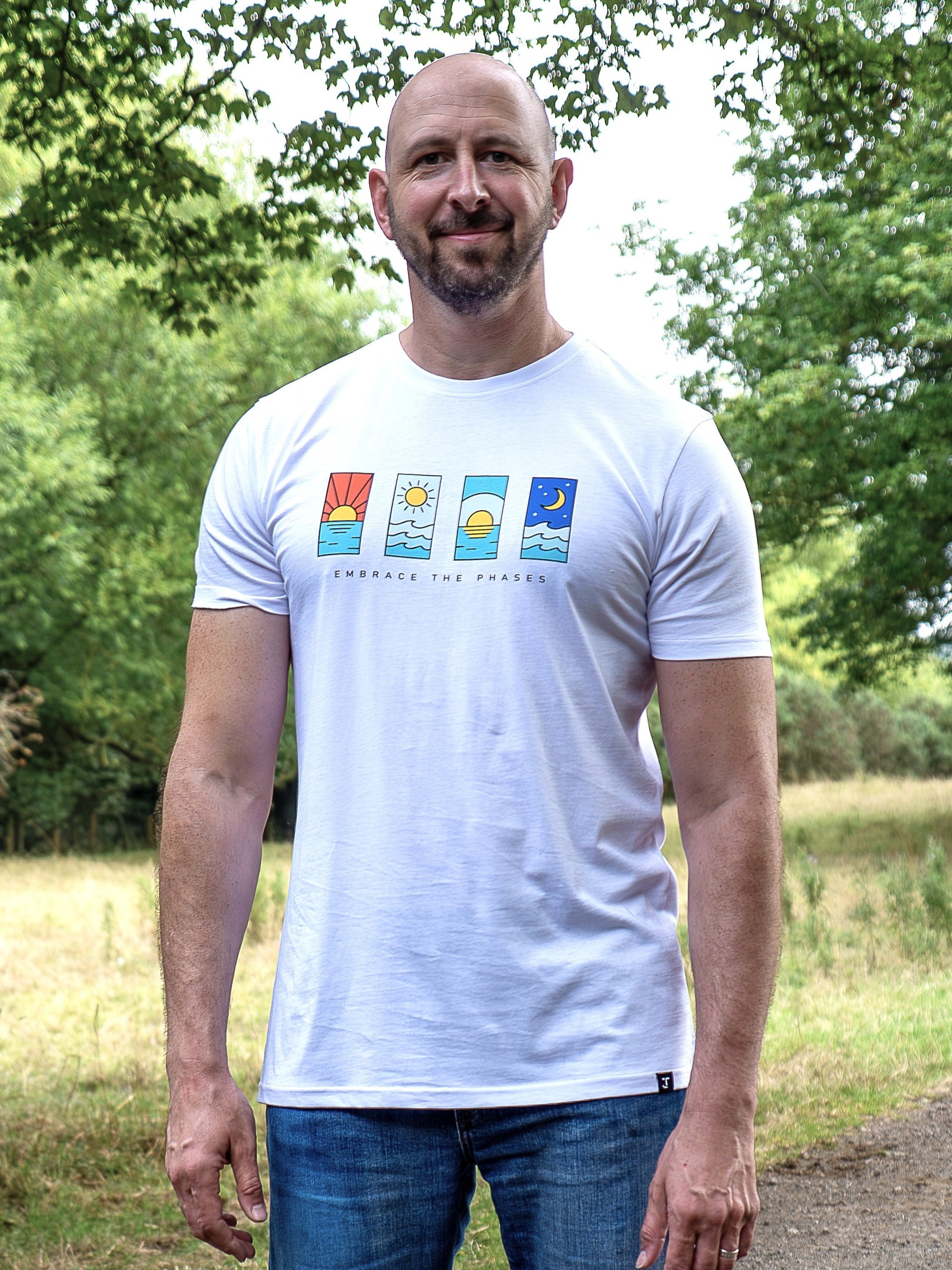 An upper body shot of a tall slim guy in a park wearing an XL tall and slim fitting graphic t-shirt in white.