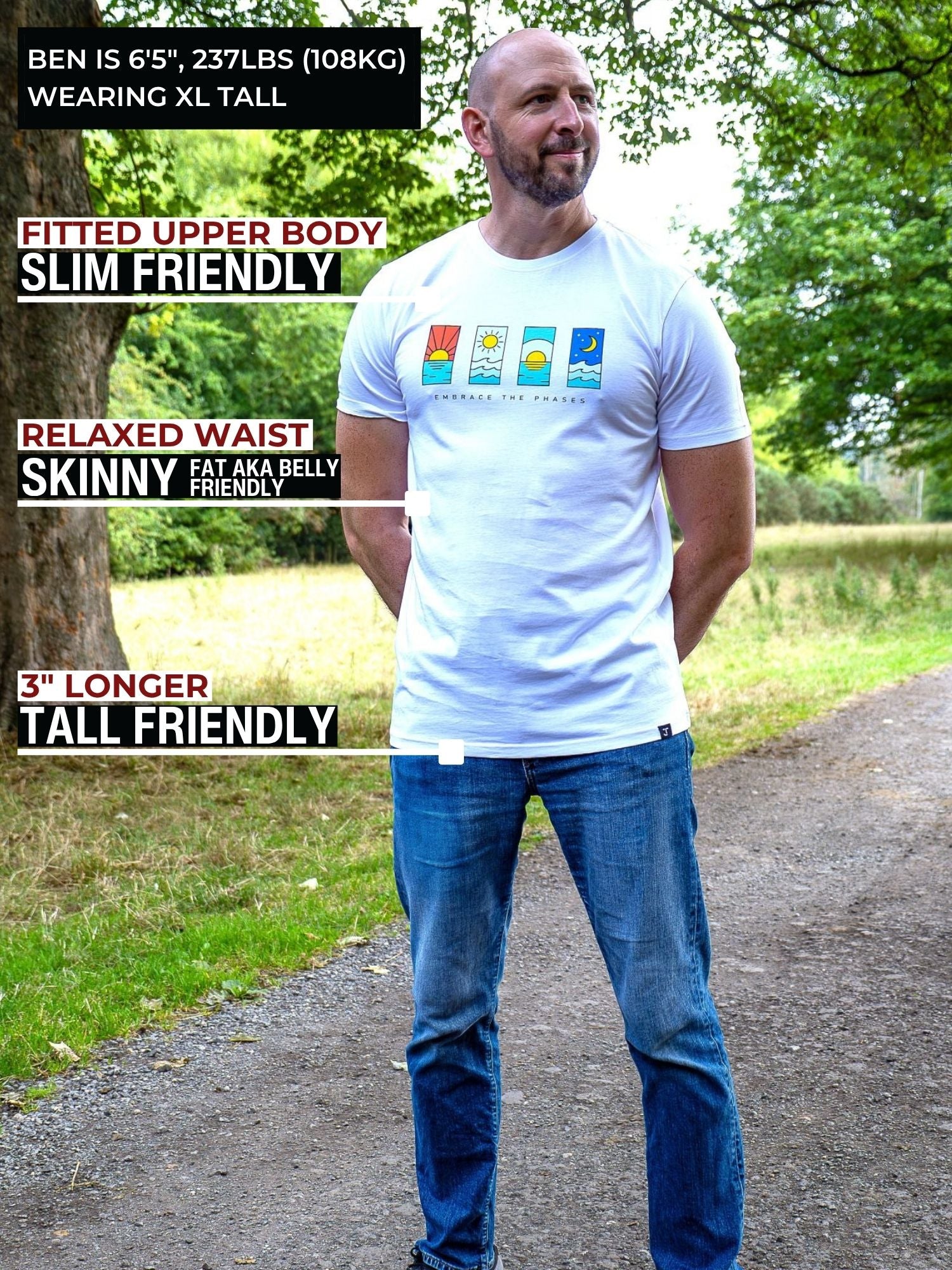 A tall man wearing a white graphic t-shirt and blue jeans stands on a dirt path outdoors with trees in the background. Text overlays on the left describe the t-shirt's slim fit and extra long length on a 6'5" model.