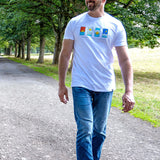 A tall man walking on a gravel path in a park, wearing a white t-shirt with a colorful graphic print and blue jeans.