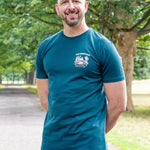 An upper body shot of a tall slim guy in a park wearing an XL tall and slim fitting graphic t-shirt in dark teal.