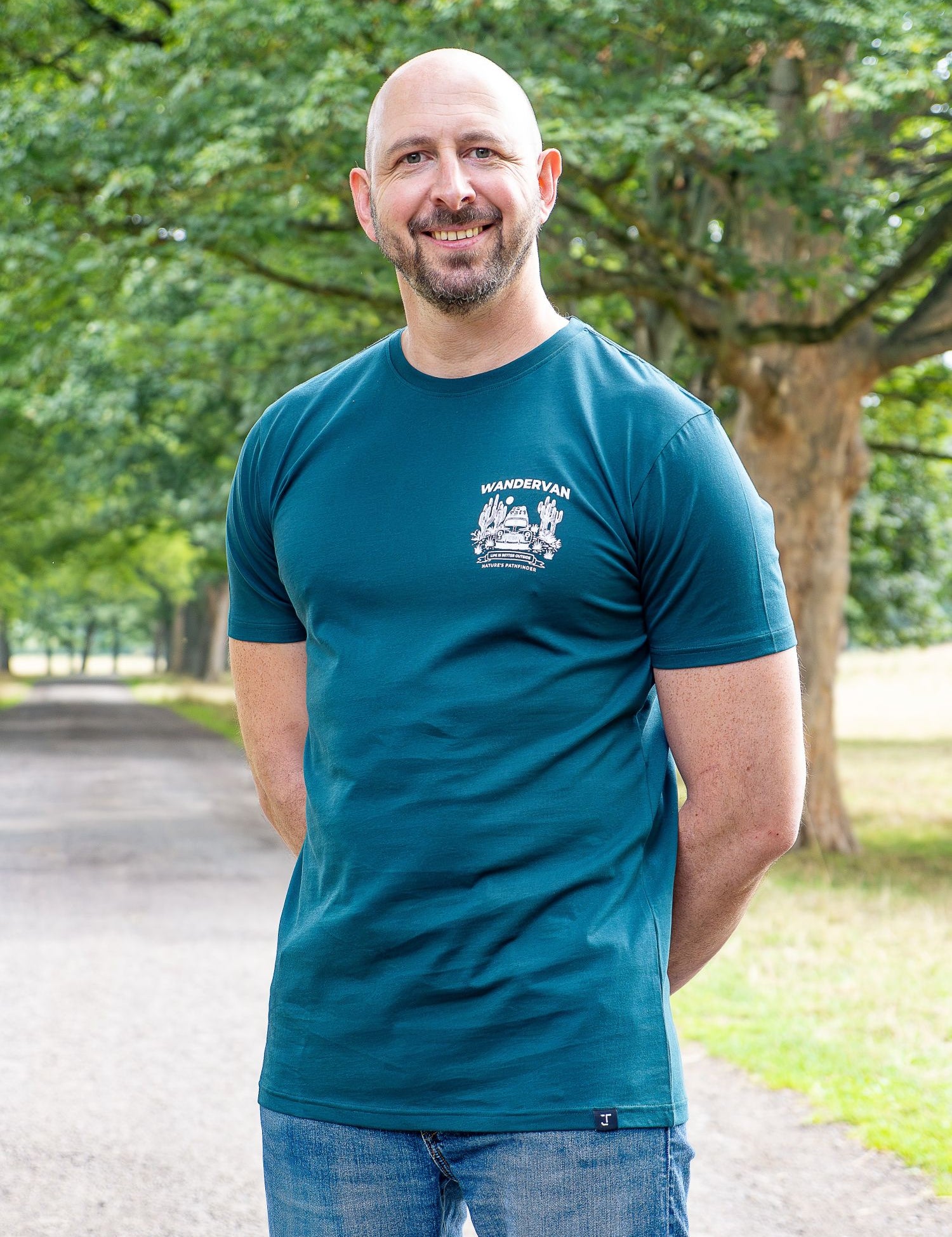 An upper body shot of a tall slim guy in a park wearing an XL tall and slim fitting graphic t-shirt in dark teal.