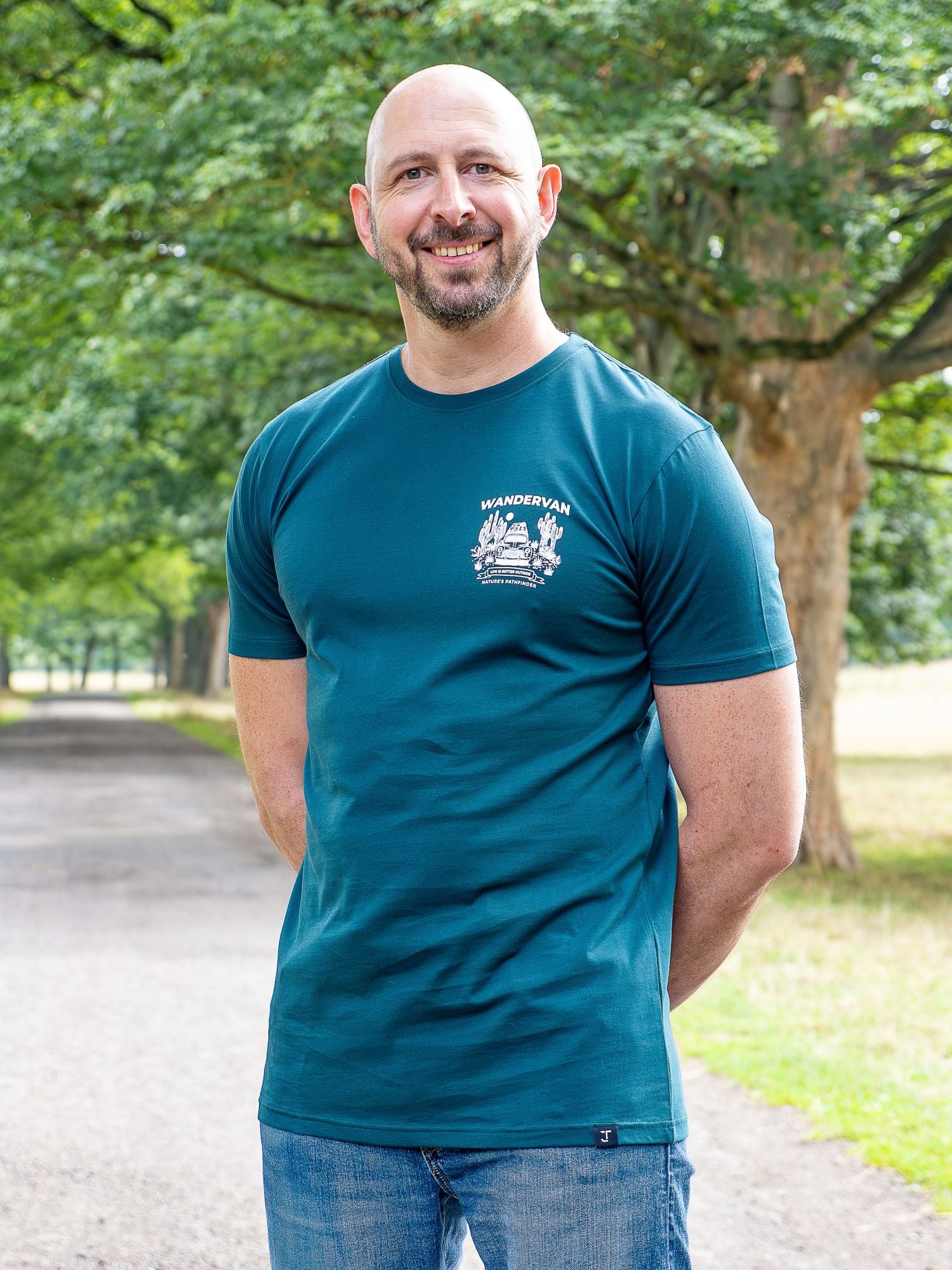 An upper body shot of a tall slim guy in a park wearing an XL tall and slim fitting graphic t-shirt in dark teal.
