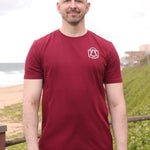 A tall and slim man standing by the sea. The smiling model is wearing a maroon extra long graphic t-shirt with a minimal tree line art design. It features a 3" longer body, 100% organic cotton, and is soft & preshrunk. This extra long tall graphic tee is ideal for tall slim men 6'2"+