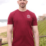 A tall and slim man standing by the sea. The smiling model is wearing a maroon extra long graphic t-shirt with a minimal tree line art design. It features a 3" longer body, 100% organic cotton, and is soft & preshrunk. This extra long tall graphic tee is ideal for tall slim men 6'2"+
