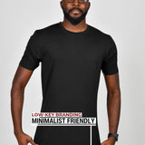 A tall slim guy wearing a large tall black heavyweight t-shirt, pulling gently down on the bottom seam to show the extra length.