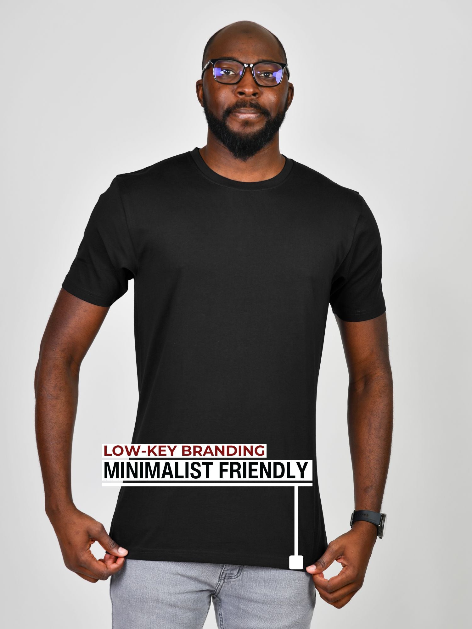 A tall slim guy wearing a large tall black heavyweight t-shirt, pulling gently down on the bottom seam to show the extra length.