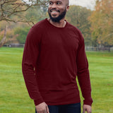 An upper body shot of a tall athletic guy wearing an XL tall maroon long sleeve t-shirt, standing in a park and smiling.