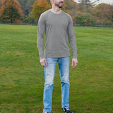 A head to toe shot of a tall athletic guy in a park wearing a light grey long sleeve tall t-shirt, looking to the left.