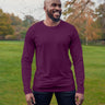 A tall athletic guy wearing a long sleeve dark purple tall t-shirt and smiling in a park while looking to the left.