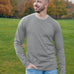 A tall and slim man standing in a park. The smiling model is wearing a light grey long-sleeve tall t-shirt. The tall light grey long-sleeve t-shirt features a 2.5" longer sleeves, 100% organic cotton, and is soft & preshrunk. The light grey long-sleeve t-shirt is ideal for tall slim men 6'2"+.