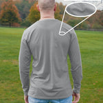A shot from behind of a tall slim guy in a park wearing an extra long sleeve long sleeve tall t-shirt in light grey.