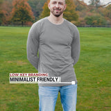 An upper body shot of a tall athletic guy standing in a park wearing a light grey extra long tall long sleeve t-shirt and showing the Just Tall minimalist monogram logo.
