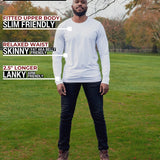 A head to toe shot of a tall athletic guy in a park wearing a white long sleeve tall t-shirt.