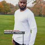 An upper body shot of a tall athletic guy standing in a park wearing a white extra long tall long sleeve t-shirt and looking down at the Just Tall minimalist monogram logo.