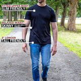 A tall man standing on a park path wearing a black fitted short-sleeve t-shirt and blue jeans, with text callouts describing the shirt's fit and length.