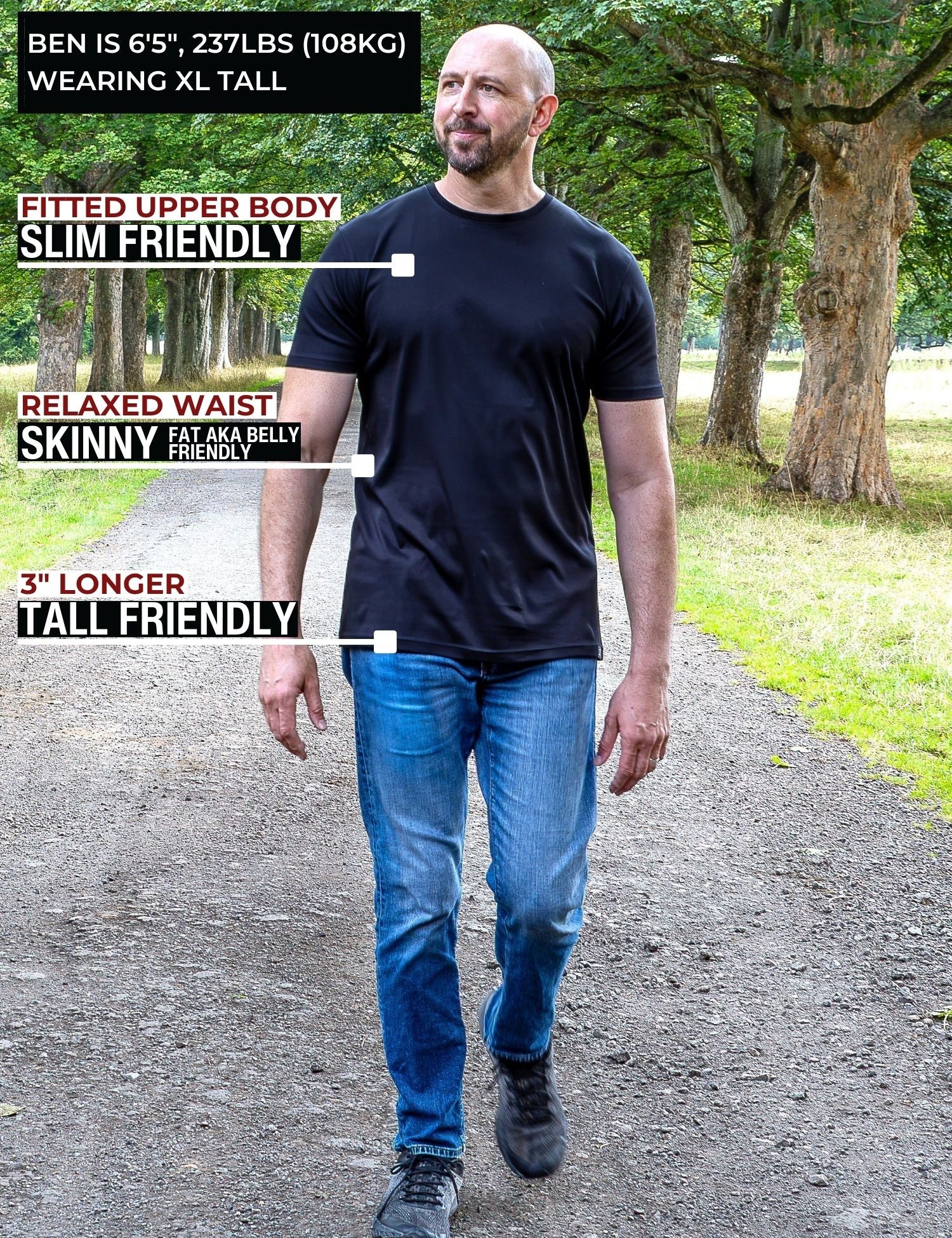 A tall man standing on a park path wearing a black fitted short-sleeve t-shirt and blue jeans, with text callouts describing the shirt's fit and length.